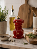 Bisetti Bird red pepper grinder with a bird on top on a kitchen counter with herbs and oil.