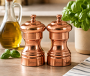 Two Bisetti copper pepper mills with a polished metallic finish, standing on a wooden table.Bisetti-USA