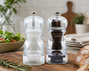 Bissett salt and pepper mills from the Milano collection on a wooden cutting board with a blurred kitchen background.