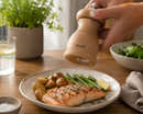 Person seasoning salmon dish with a bisetti poortofino salt grinder on a table.