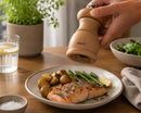 Person seasoning salmon with a Bisetti portofino pepper grinder on a dining table.