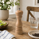Bisetti roma pepper grinder on a wooden table with a glass of water and a bowl of salad in the background.